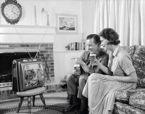 Примерно 1960: молодая пара смотрит портативный телевизор в гостиной.