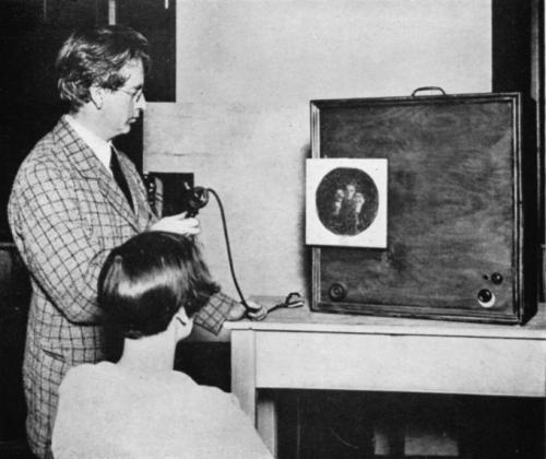 Бэрд начал экспериментировать с системами визуализации в начале 1920-х. В 1924 году он сумел передать по проводам первое контурное изображение, а к 1925 году уже был в состоянии передавать узнаваемые человеческие лица. В 1926 году он открыл первый в мире телецентр, названный им 2TV.На фото: Джон Лоуги Бэрд перед экраном одного из первых телепередатчиков («прибор беспроводного видения»).