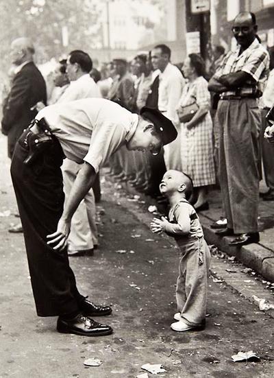 1958
Издание: Washington (DC) Daily News
Автор: Уильям Си Биалл (William C. Beall)
На снимке запечатлен полицейский, терпеливо объясняющий двухлетнему мальчику, который попытался пересечь улицу во время парада, возможные последствия его поступка.